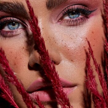 primer plano de mujer maquillada con en tonos ciruela sosteniendo unas ramas rojas