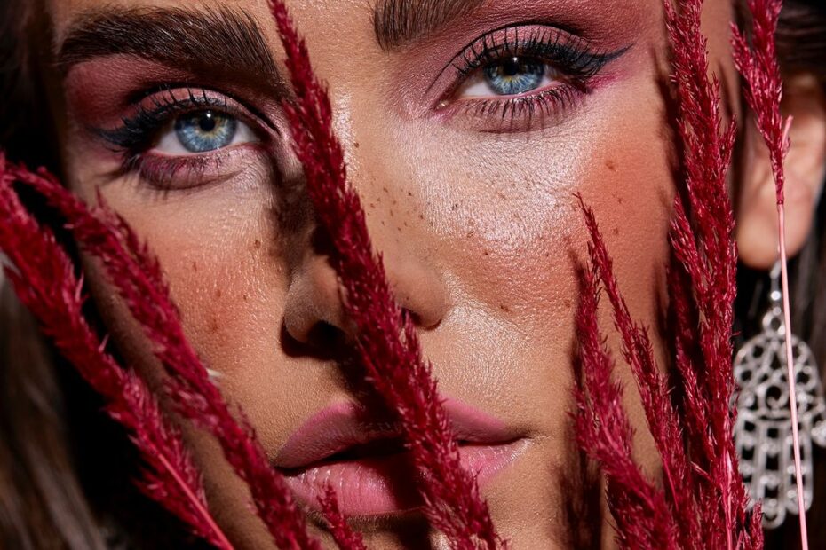 primer plano de mujer maquillada con en tonos ciruela sosteniendo unas ramas rojas